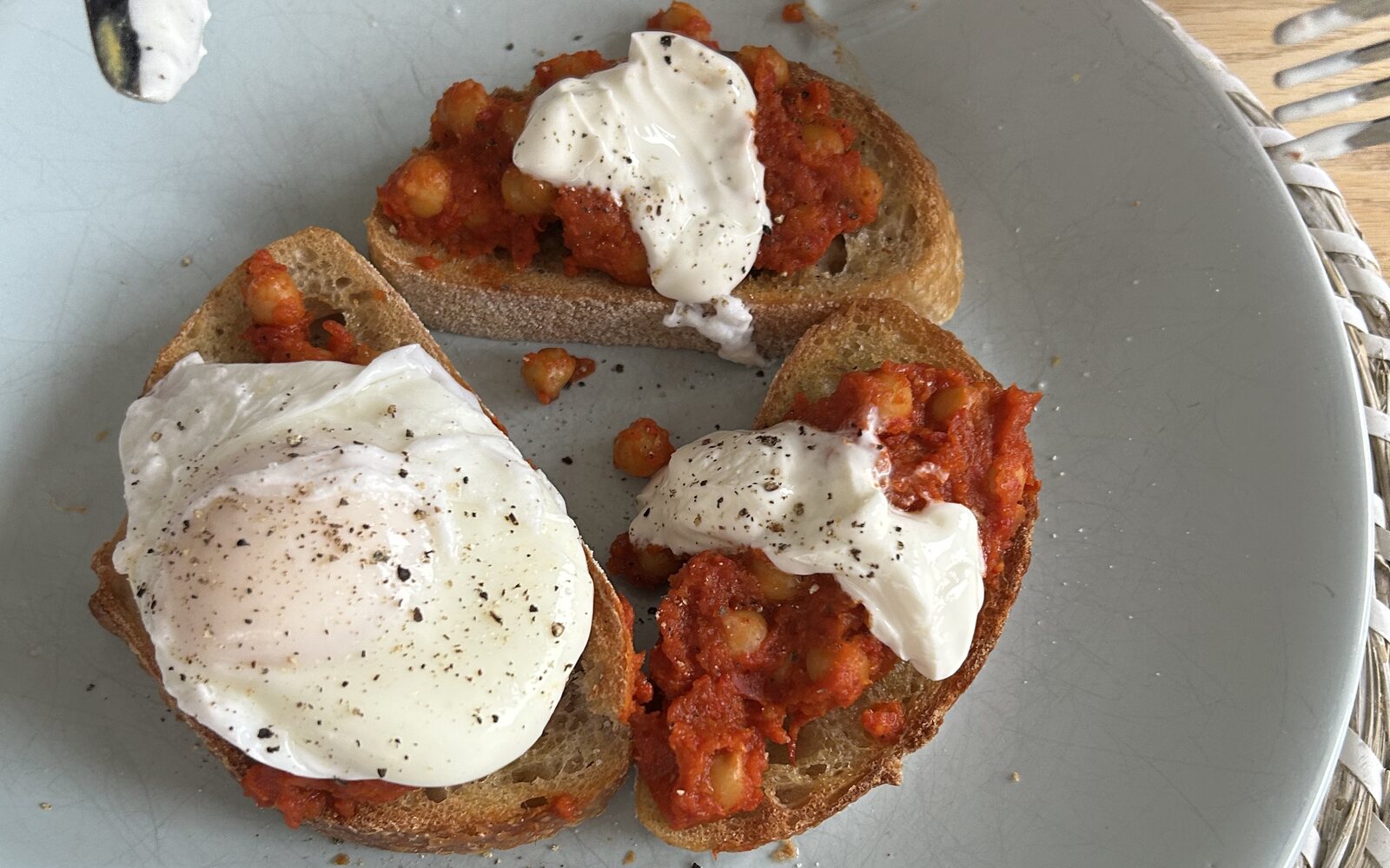 Three slices of sourdough topped with chickpeas in tomato sauce, one with a poached egg and two with Greek yoghurt