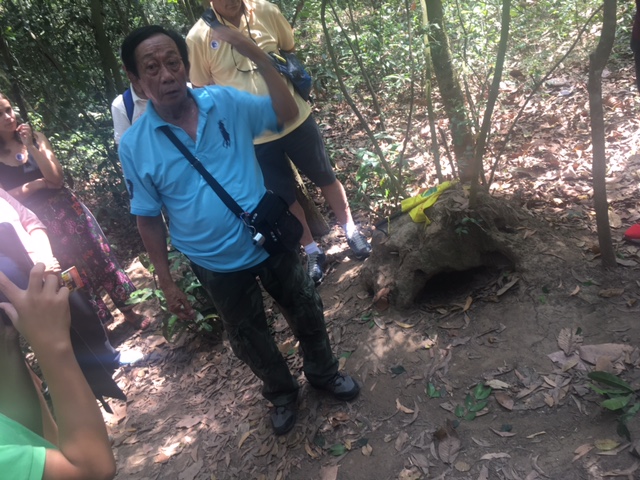 Our guide demonstrating a concealed tunnel entrance at Cu Chi